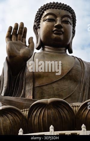 Un primo piano della statua in bronzo di Tian Tan Buddha (grande Buddha) a Ngong Ping, che mostra la mano destra sollevata, la faccia serena e l'ingegno intricatamente intagliato Foto Stock