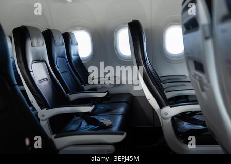 File di sedili aerei non occupati con cinture di sicurezza, poggiatesta e tavolini visibili all'interno di una moderna cabina per aeromobili commerciali a fusoliera stretta Foto Stock