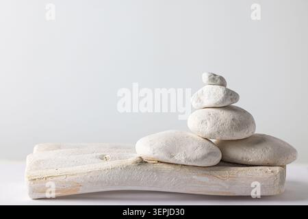 Pila di ciottoli bianchi su un vassoio in legno rustico su sfondo bianco con spazio per le copie per l'equilibrio del benessere della spa Foto Stock