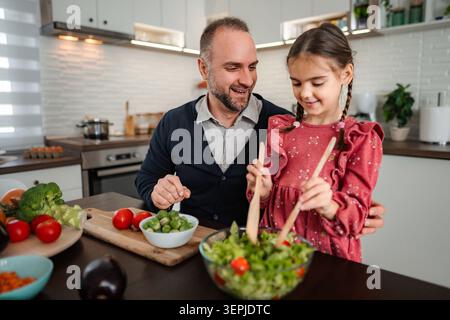 Padre e figlia cucinano insalata sana in cucina Foto Stock