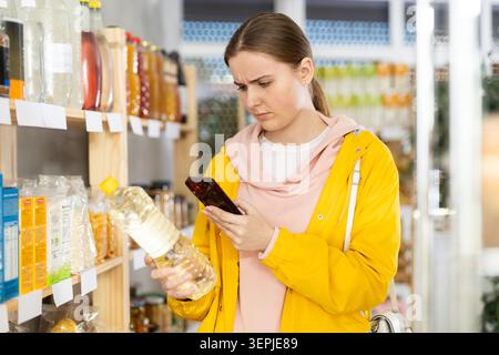 Donna scansiona un codice QR sui prodotti sugli scaffali dei supermercati per controllare le date di scadenza Foto Stock