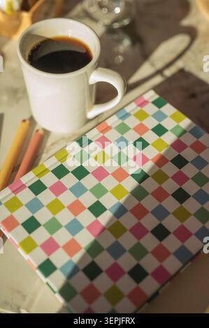 Una tazza di caffè e un diario personale colorato alla luce del sole mattutino Foto Stock