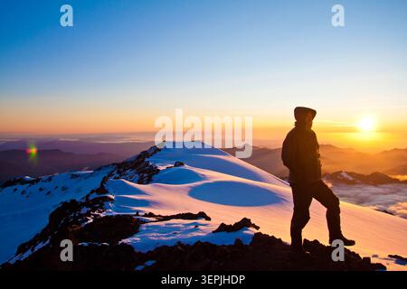 L'uomo gode di una vista all'alba dalla cima innevata della montagna Foto Stock