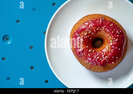Una ciambella rosa smaltata su un tavolo blu Foto Stock