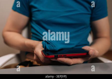 Immagine ritagliata verticale di una persona in maglietta che pulisce lo schermo dello smartphone, dimostrando la cura quotidiana dei dispositivi e la manutenzione ordinaria per schermi touch puliti Foto Stock
