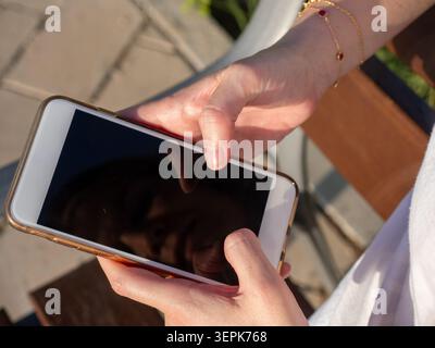 Donna con le mani in mano con uno smartphone, toccando lo schermo, coinvolgendo la tecnologia e la comunicazione moderne Foto Stock