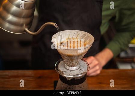 Primo piano di un barista che versa acqua calda da un bollitore a collo d'oca in un filtro per caffè Foto Stock