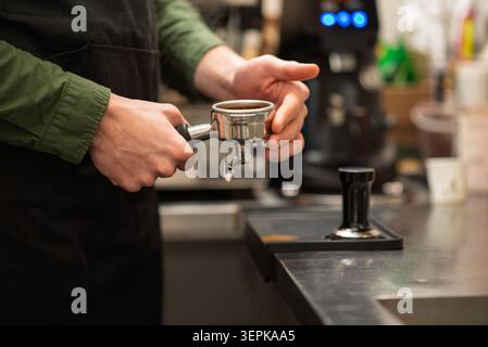 Primo piano di un barista che tiene in mano un portafiltro pieno di fondi di caffè Foto Stock