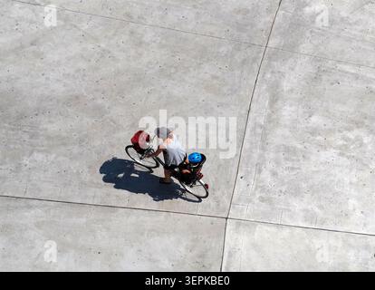 Vista dall'alto di una mamma in bicicletta con suo figlio con un casco seduto sulla sella dietro. Strada in cemento sullo sfondo. Persone irriconoscibili Foto Stock