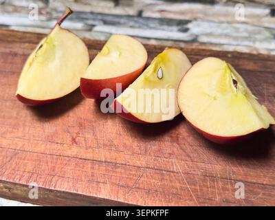 fette di mela rossa sul tagliere in legno graffiato, frutta fresca matura e succosa con polpa e semi, dieta sana con spazio per copiare Foto Stock