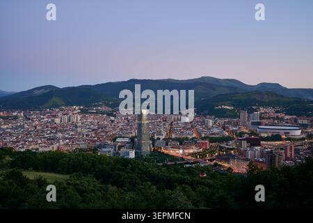 Bilbao di notte, il paesaggio urbano di Bilbao da un alto punto panoramico, con il moderno grattacielo e lo stadio illuminato di sera con le montagne circostanti Foto Stock