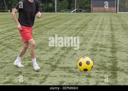 Un giocatore di calcio maschile si allena su un campo di calcio concentrandosi sul controllo della palla e praticando esercizi di tiro durante una sessione all'aperto. Foto Stock