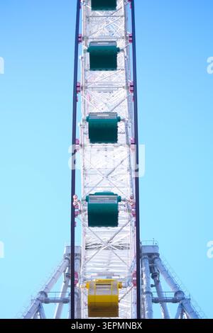Una maestosa ruota panoramica che raggiunge il cielo azzurro con le sue auto vuote verdi e gialle che aspettano i piloti Foto Stock