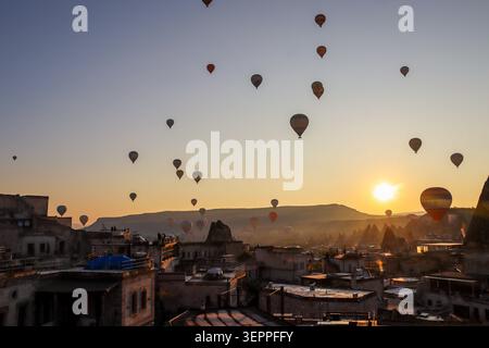 Questa immagine cattura una vista mozzafiato delle mongolfiere che si innalzano sulla Cappadocia mentre il sole sorge, mostrando il paesaggio unico. Foto Stock
