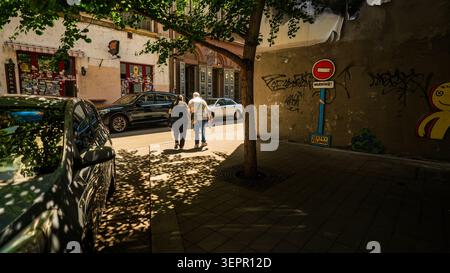Budapest, Ungheria - 4 giugno 2026: Tranquilla scena stradale di Budapest con auto parcheggiate, due pedoni, ombre degli alberi, muri di graffiti e architettura europea Foto Stock