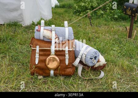 Zaino vintage in pelle in stile militare con coperte arrotolate e un pesce, esposto sull'erba in un ambiente all'aperto, che evoca un tema storico Foto Stock