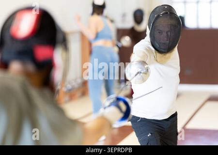 Un gruppo di recinti si allena in duelli e fa uscire i colpi sui cuscini in palestra Foto Stock