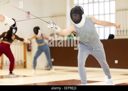Un gruppo di recinti si allena in duelli e fa uscire i colpi sui cuscini in palestra Foto Stock