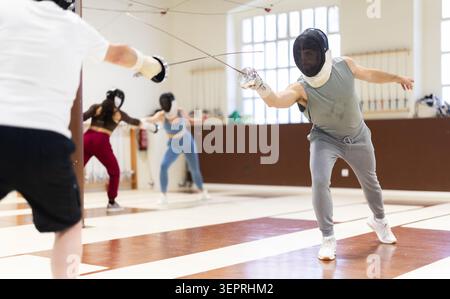 Un gruppo di recinti si allena in duelli e fa uscire i colpi sui cuscini in palestra Foto Stock