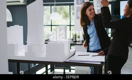 Team di architetti che condividono cinque alti risultati dopo aver fatto progressi nel loro progetto di ristrutturazione, dipendenti di agenzie immobiliari che collaborano per eseguire piani di progetto, esperti CAD che progettano progetti. Foto Stock