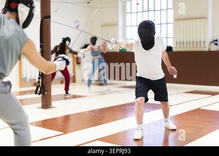 Un gruppo di recinti si allena in duelli e fa uscire i colpi sui cuscini in palestra Foto Stock