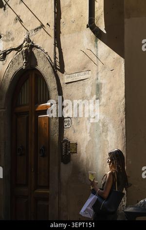 Donna appoggiata a un muro di casa con drink e shopping bag, Firenze, Toscana, Italia Foto Stock