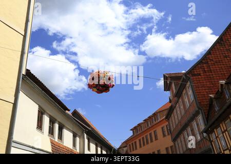 Guardando in alto in un vicolo storico, dove una palla artistica di fiori colorati galleggia liberamente tra le facciate della casa. Il tradizionale mezzo legno Foto Stock
