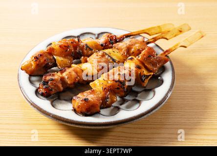 Tre spiedini di pollo Yakitori giapponesi su piatto in ceramica su tavolo in legno Foto Stock
