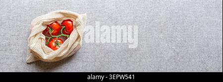 Banner Web, pomodori freschi in un sacchetto a rete riutilizzabile su sfondo grigio con spazio per le copie. Concetto di shopping sostenibile. Foto Stock