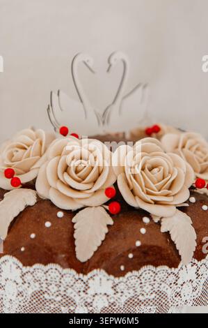 Uno shot ravvicinato di un tradizionale pane da sposa splendidamente decorato, adornato con rose fondenti beige artigianali, piccoli frutti di bosco rossi e un elegante Foto Stock