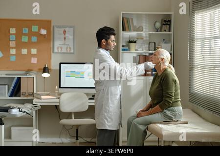 Donna anziana in visita al medico e in corso di esame del collo in clinica Foto Stock