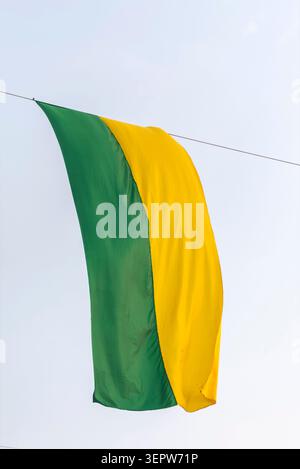 Il colore brasiliano bandiera gialla e verde è appeso su un cielo blu isolato Foto Stock