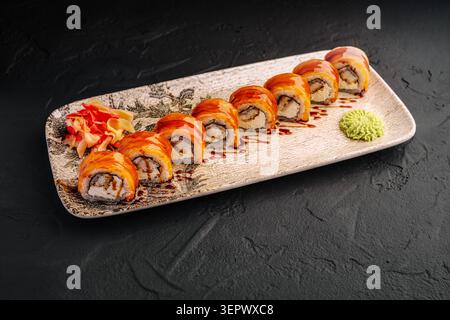 Un piatto mostra diversi rotoli di sushi allineati in modo ordinato. Gli involtini hanno il pesce sopra e sono accompagnati da piccoli mucchi di wasabi e zenzero. Questa scena mostra una tipica presentazione del cibo giapponese. Foto Stock