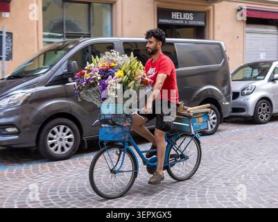 L'uomo asiatico che porta un grande mazzo di fiori corre in bicicletta su una strada a Parma, Italia Foto Stock