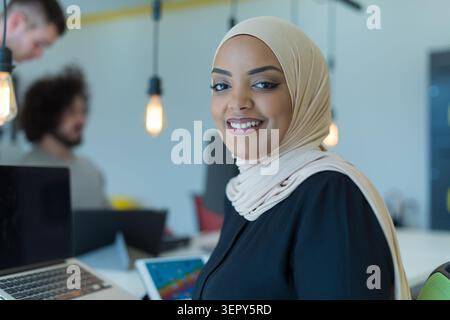 Ritratto ravvicinato di una giovane donna musulmana di successo che indossa un hijab beige e una camicetta nera, sorridendo direttamente alla fotocamera. Nel backg della messa a fuoco morbida Foto Stock