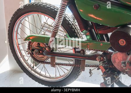 La ruota posteriore e le sospensioni delle motociclette d'epoca presentano elementi del telaio arrugginiti, battistrada degli pneumatici usurati e usura visibile grazie alla molla elicoidale rossa e alla trasmissione a catena Foto Stock