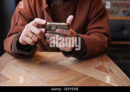 Una giovane donna controlla il proprio smartphone mentre si siede a un tavolo in un bar Foto Stock