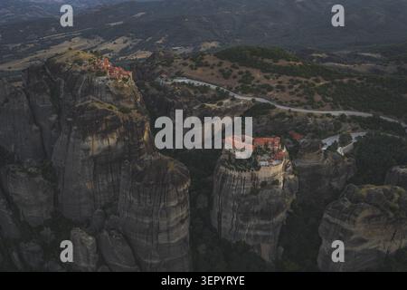 Vista aerea degli storici monasteri di Meteora arroccati su enormi pilastri di roccia circondati da lussureggianti colline verdi e strade tortuose a Trikala, in Grecia. Foto Stock