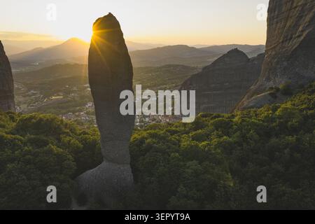 Vista aerea della colonna rocciosa di Adrachti al tramonto con il sole che splende dietro la guglia di pietra e il villaggio di Kastraki nella valle di Trikala, GR Foto Stock