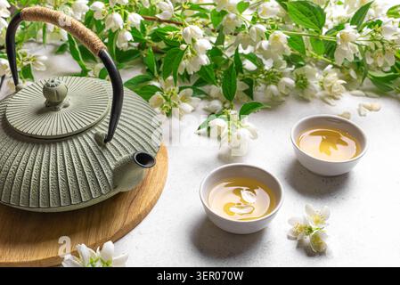 Tè verde giapponese con gelsomino in teiera in ghisa e tazze da tè su sfondo bianco. Tè al gelsomino naturale e rami in fiore. Foto Stock