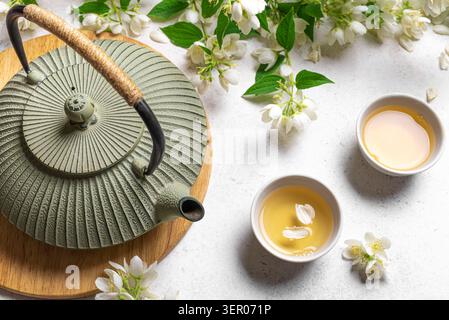Tè verde giapponese con gelsomino in teiera in ghisa e tazze da tè su sfondo bianco. Tè al gelsomino naturale e rami in fiore. Foto Stock