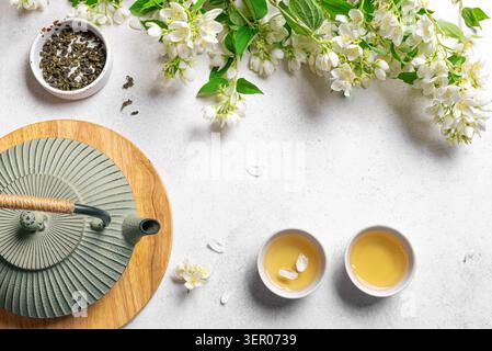 Tè verde con gelsomino in teiera in ghisa e tazze da tè su sfondo bianco, vista dall'alto, spazio fotocopie. Tè al gelsomino naturale e fiori, modello. Foto Stock