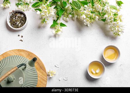 Tè verde con gelsomino in teiera e tazze da tè su sfondo bianco, vista dall'alto, spazio copia. Tè al gelsomino naturale e fiori. Foto Stock