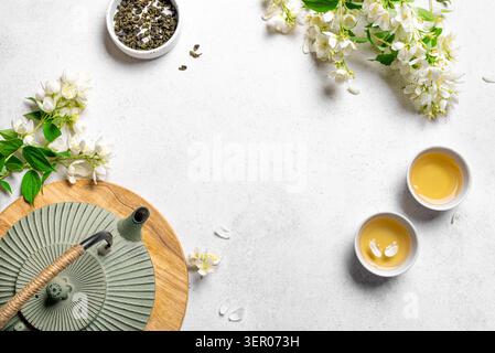 Tè verde con gelsomino in teiera e tazze da tè su sfondo bianco, vista dall'alto, spazio copia. Tè al gelsomino naturale e fiori. Foto Stock