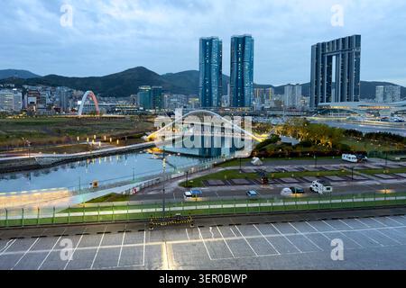 Skyline illuminato della città e ponte ad arco pedonale sul canale al crepuscolo di Busan, Corea del Sud Foto Stock