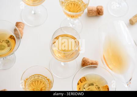 I bicchieri da vino bianchi con liquido dorato e sugheri sparsi sono disposti su uno sfondo chiaro, simboleggiando la celebrazione, il lusso e gli incontri festivi Foto Stock