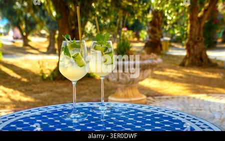 Rinfrescanti cocktail estivi di cetrioli e menta in bicchieri da vino su un tavolo piastrellato nel giardino soleggiato. Foto Stock