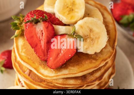 Pancake con banana, fragole e miele da vicino. Cibo mattutino, colazione estiva. Giornata con frittelle dolci o ricetta Maslenitsa Foto Stock