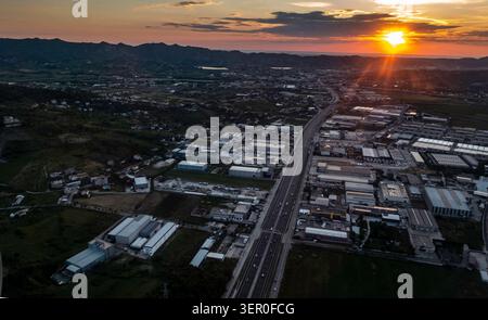 Vista aerea di un paesaggio autostradale durante l'avvicinamento all'aeroporto di Tirana, Albania, scattata al tramonto con le montagne visibili in lontananza. Foto Stock