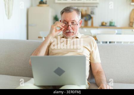 Un uomo anziano di mezza età felice con un computer portatile che parla in videochiamata con amici e familiari. Vecchio nonno anziano maturo che si diverte a parlare con i bambini grandi online. Utilizzo della tecnologia moderna di vecchia generazione Foto Stock